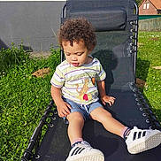 Maël participe au concours pour gagner de l'argent avec cette photo : boy, child, clothing, curlyhair, face, footwear, furniture, grass, hair, head, male, outdoors, person, photography, plant, portrait, shoe, shorts, sitting, sneaker
