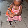 checkered, child, cute, dress, floor, girl, hair_clips, indoor, natural_light, orange, person, pink, playful, pose, purse, sandal, tile_floor, toddler, white_sandal, young_child