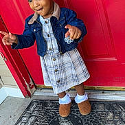 Harlee is registered to the contest to win money with this photo: toddler, child, girl, denim_jacket, plaid_dress, hair_beads, red_door, doormat, outdoor, concrete, pointing, smiling, socks, shoes, playful, portrait, standing, person, fashion, casual