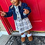 toddler, child, girl, denim_jacket, plaid_dress, hair_beads, red_door, doormat, outdoor, concrete, pointing, smiling, socks, shoes, playful, portrait, standing, person, fashion, casual