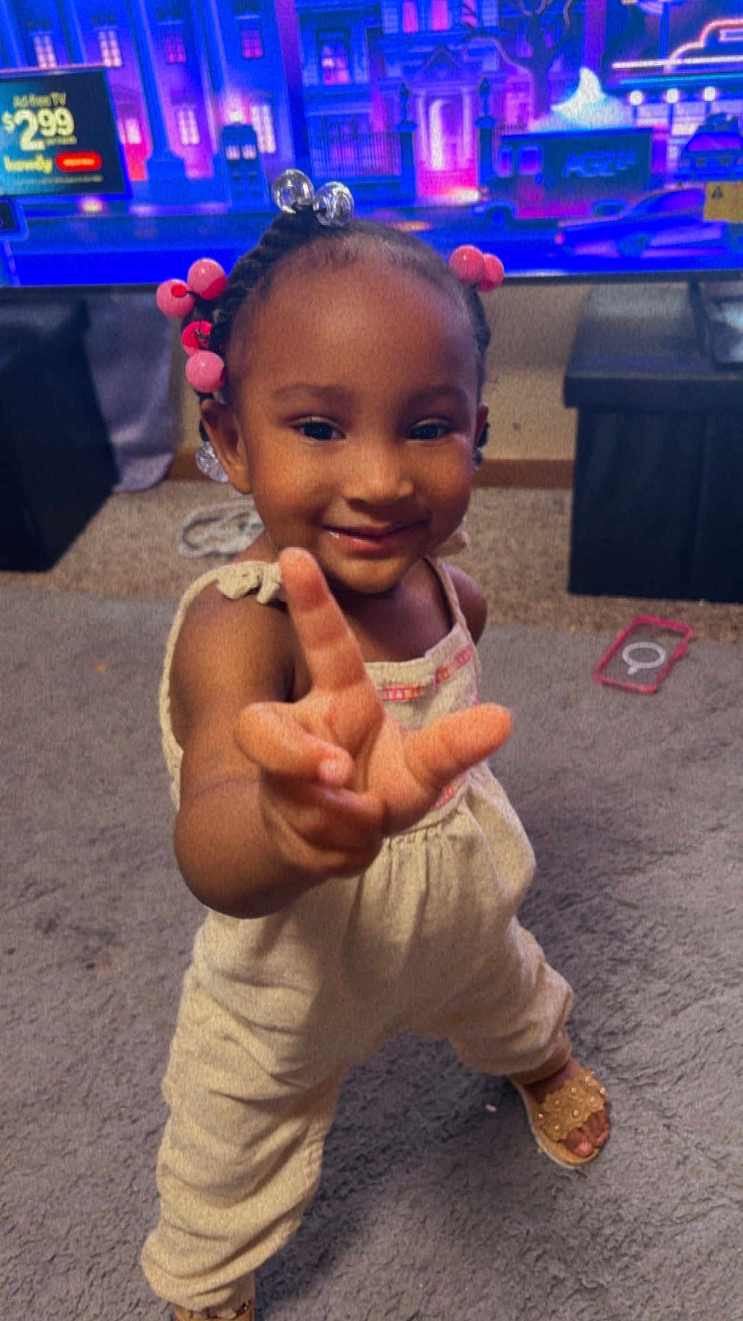 Harlee joined the competition — help win amazing prizes! toddler, child, smiling, indoor, carpet, playful, hand, gesture, clothing, hair_beads, footwear, television, furniture, room, person, cute, happy, portrait, young_child, home