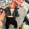 Aurora-Grace joined the competition — help win amazing prizes! baby, infant, denim_jacket, black_pants, tattoo, hand, blanket, diaper, plastic_bag, floor, soft_surface, lying_down, clothing, person, skin, foot, head, cute, indoor, baby_care