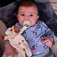 Léo participe au concours pour gagner de l'argent avec cette photo : baby, pacifier, plush_toy, giraffe_toy, mickey_mouse, blue_clothing, pillow, infant, cute, child, soft_toy, relaxed, indoor, portrait, sleepwear, hand, face, young_child, couch, comfort