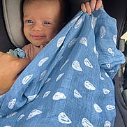 Grayson is registered to the contest to win money with this photo: baby, child, blanket, blue, car_seat, pacifier, hand, smile, face, person, infant, comfort, cozy, pattern, clothing, cute, young, cute_expression, indoor, closeup