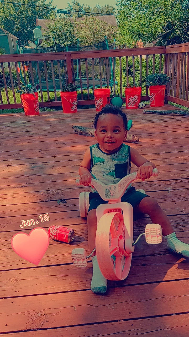 A'Kai is registered to the contest to win money with this photo: baby_toddler_clothing, beauty, child, event, fun, happy, hardwood, joy, leisure, orange, person, pink, plant, recreation, sitting, smile, t_shirt, toddler, toy, tree