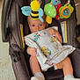 Max is registered to the contest to win money with this photo: baby, car_seat, blanket, stuffed_toy, mobile, bee_toy, mushroom_toy, sock, infant, child, toy, cute, blue_eyes, patterned_fabric, floor, indoor, colorful, holding, sitting, pacifier