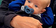 Max is registered to the contest to win money with this photo: baby, pacifier, blanket, bear_pattern, adult_hand, ring, jacket, outdoor, bench, chain_link_fence, cloudy_sky, person, child, blue_eyes, face, holding, casual_clothing, closeup, portrait, comfort