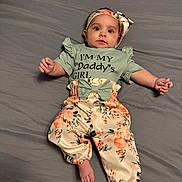 Persephone joined the competition — help win amazing prizes! baby, child, infant, portrait, lying_down, bed, bedspread, floral_outfit, dress, headband, bow, wide_eyed, looking_at_camera, arms, hands, barefoot, indoor, home, gray_background, fashion