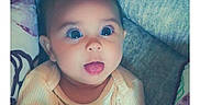 Persephone is registered to the contest to win money with this photo: baby, bed, blanket, child, closeup, clothing, cozy, home, indoors, infant, open_mouth, pastel_colors, photograph, portrait, sitting, smiling, surprised, timestamp, wide_eyes, yellow_outfit