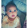 Persephone is registered to the contest to win money with this photo: baby, infant, child, portrait, sitting, wide_eyes, open_mouth, smiling, blanket, bed, clothing, yellow_outfit, indoors, home, cozy, closeup, photograph, timestamp, pastel_colors, surprised