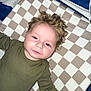 Ryder joined the competition — help win amazing prizes! baby, checkered_pattern, child, close_up, cozy, curly_hair, cushion, expression, face, hand_holding, indoor, infant, looking_at_camera, lying_down, olive_green_clothing, person, pink_nails, portrait, soft_lighting, young_child