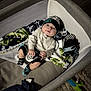 baby, blanket, carpet, child, clothing, comfort, cushion, cute, floor, hat, indoor, infant, lying_down, person, playpen, smile, socks, soft_toys, toys, wood_floor