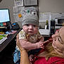 Ryder is registered to the contest to win money with this photo: baby, clothing, computer, curious, cute, desk, furniture, hat, holding, indoor, infant, office, paper, person, phone, printer, smile, technology, woman, workspace