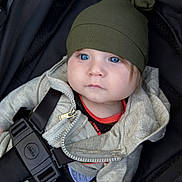Ryder is registered to the contest to win money with this photo: baby, child, stroller, hat, blue_eyes, jacket, zipper, straps, clothing, infant, person, portrait, cute, casual_wear, seatbelt, sitting, young, face, headwear, outdoor