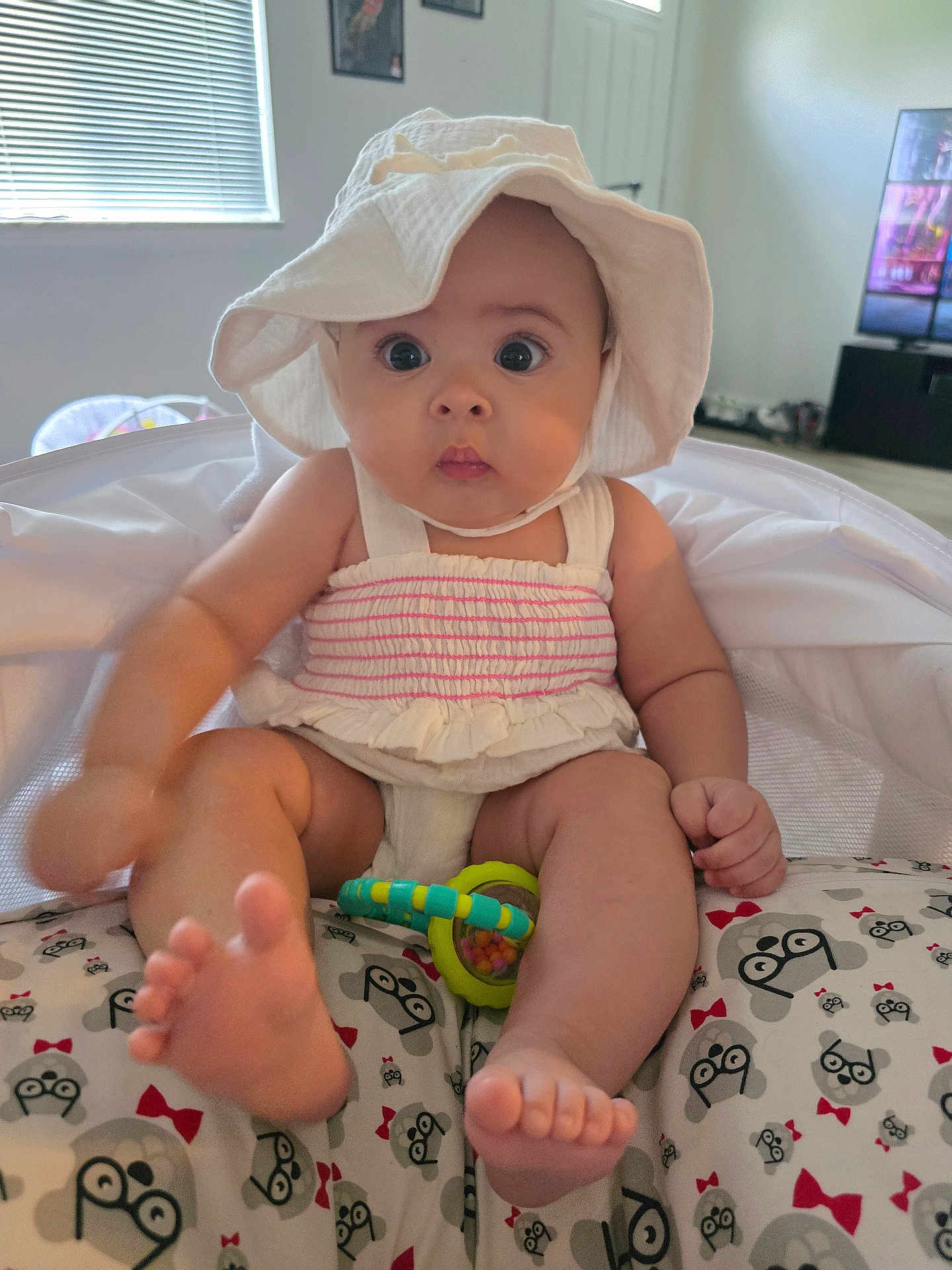 Geneva joined the competition — help win amazing prizes! baby, child, hat, white_hat, rattle, cushion, patterned_cushion, monkey_pattern, indoor, room, window, furniture, foot, hand, clothing, infant, cute, wide_eyes, sitting, toy