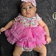 Geneva joined the competition — help win amazing prizes! baby, infant, pink_tutu, headband, bow, lying_down, curious_expression, chubby_cheeks, onesie, patterned_clothing, barefoot, indoor, soft_surface, cute, child, portrait, small_person, baby_girl, fabric, texture