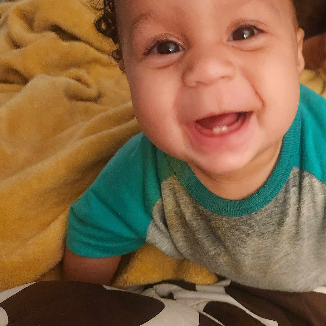 Joel joined the competition — help win amazing prizes! baby, smiling, curly_hair, blanket, indoor, happy, face, child, cute, portrait, clothing, toddler, cozy, infant, home, person, young_child, expression, warm, cheerful