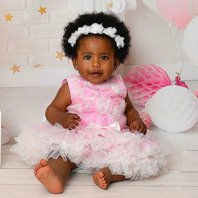 Julia joined the competition — help win amazing prizes! baby, balloons, barefoot, celebration, child, curly_hair, cute, decorations, festive, floor, girl, headband, indoor, pastel_colors, pink_dress, portrait, roses, ruffled_skirt, sitting, smiling