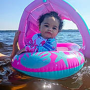 Miah'Ja is registered to the contest to win money with this photo: toddler, child, inflatable_float, water, lake, sunny, curly_hair, pink, blue, swimwear, summer, outdoor, water_safety, person, floating, hand, reflection, vacation, relaxation, nature
