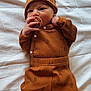 baby, infant, pacifier, hat, brown_outfit, croissant_pattern, knitted_socks, white_blanket, lying_down, cute, cozy, sleepwear, child, newborn, soft_texture, warm_clothing, indoors, portrait, adorable, resting