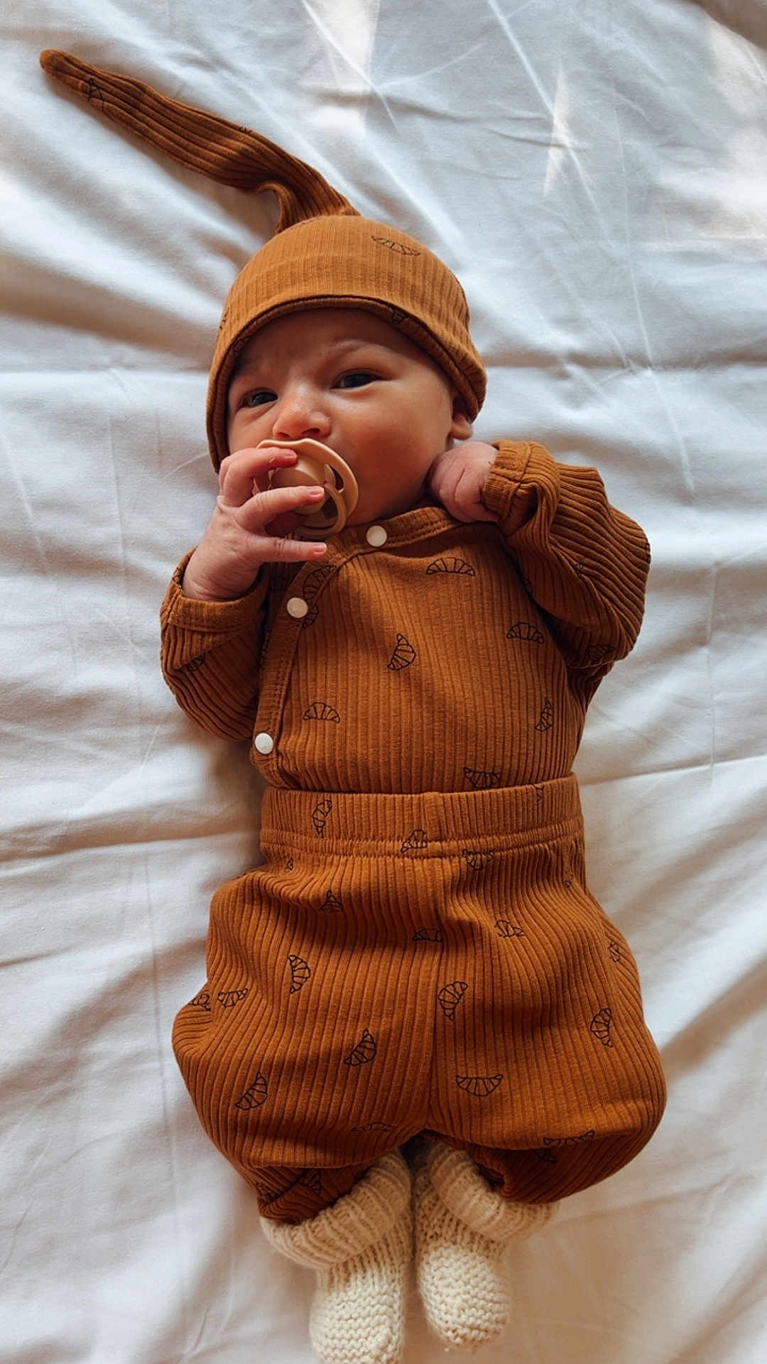 Joshua a rejoint le concours — aidez-le/la à gagner de superbes lots ! baby, infant, pacifier, hat, brown_outfit, croissant_pattern, knitted_socks, white_blanket, lying_down, cute, cozy, sleepwear, child, newborn, soft_texture, warm_clothing, indoors, portrait, adorable, resting