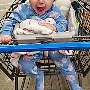 Nylah joined the competition — help win amazing prizes! baby, child, shopping_cart, hat, beanie, blue_onesie, blanket, store_aisle, floor, smiling, happy, infant, clothing, person, retail, indoor, face, cute, holding, joyful