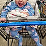 baby, child, shopping_cart, hat, beanie, blue_onesie, blanket, store_aisle, floor, smiling, happy, infant, clothing, person, retail, indoor, face, cute, holding, joyful