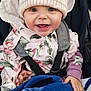 baby, child, smiling, hat, beanie, jacket, floral_pattern, blanket, stroller, bundle, happy, cute, face, hands, warm_clothing, hood, outside, person, infant, cozy