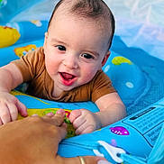 Jaysel joined the competition — help win amazing prizes! baby, infant, child, smiling, happy, portrait, face, eyes, open_mouth, short_hair, brown_shirt, blue_playmat, activity_center, toy, colorful, indoor, close_up, adult_hand, playtime, family
