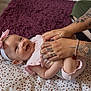 adult_hands, baby, bracelet, fingers, floor, happy, headband, indoor, infant, laughing, person, pink_clothing, playful, polka_dot_mat, purple_carpet, ring, skin, smiling, striped_wall, tattoos