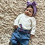 baby, child, smiling, headband, purple_bow, white_sweater, blue_jeans, belt, carpet, fluffy, indoor, cute, infant, portrait, person, footwear, white_shoes, happy, lying_down, playful