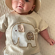 Justin is registered to the contest to win money with this photo: baby, infant, hat, elephant, shirt, clothing, white_pants, blanket, lying_down, cute, child, face, portrait, indoors, soft_light, fabric, texture, smiling, person, small_hand