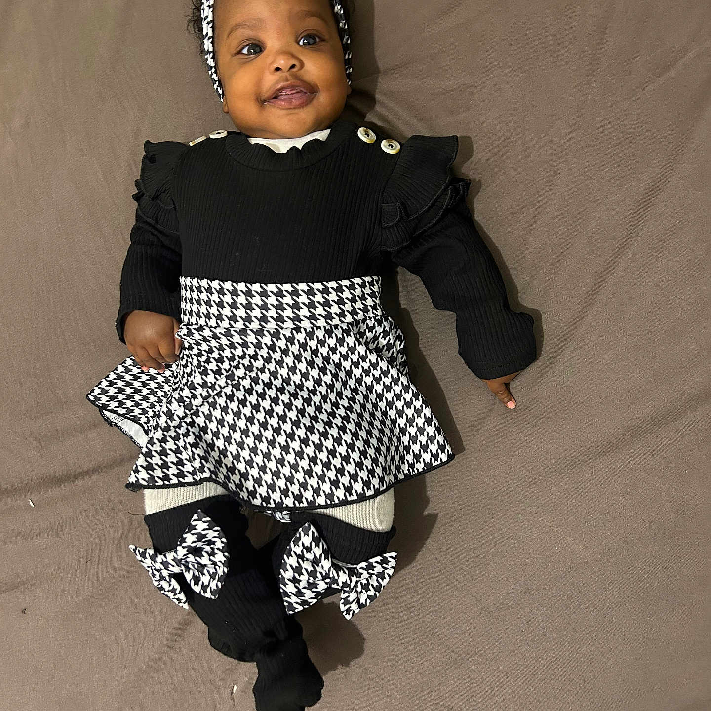 Lalyah participe au concours pour gagner de l'argent avec cette photo : baby, bed, black_clothing, blanket, bow, child, cute, fashion, happy, headband, houndstooth_pattern, indoors, infant, lying_down, person, portrait, smiling, sock, toddler, white_clothing