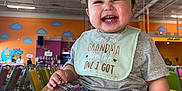 Nathan joined the competition — help win amazing prizes! baby, bib, casual_clothing, child, clouds, colorful_chairs, cute, dinosaur_mural, expression, feet, hands, happy, indoor, infant, person, plaid_shorts, play_area, short_sleeves, smiling, wooden_table