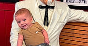 Stetson joined the competition — help win amazing prizes! baby, child, infant, smiling, sitting, statue, colonel_sanders, restaurant, bench, wood, red_wall, white_suit, bow_tie, glasses, framed_pictures, indoor, portrait, casual_clothing, sneakers, funny_pose