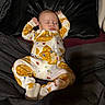 baby, infant, sleeping, bed, bedding, onesie, clothing, portrait, indoors, face, eyes_closed, peaceful, lying_down, arms_raised, patterned_clothing, dark_background, home, photography, cozy, newborn