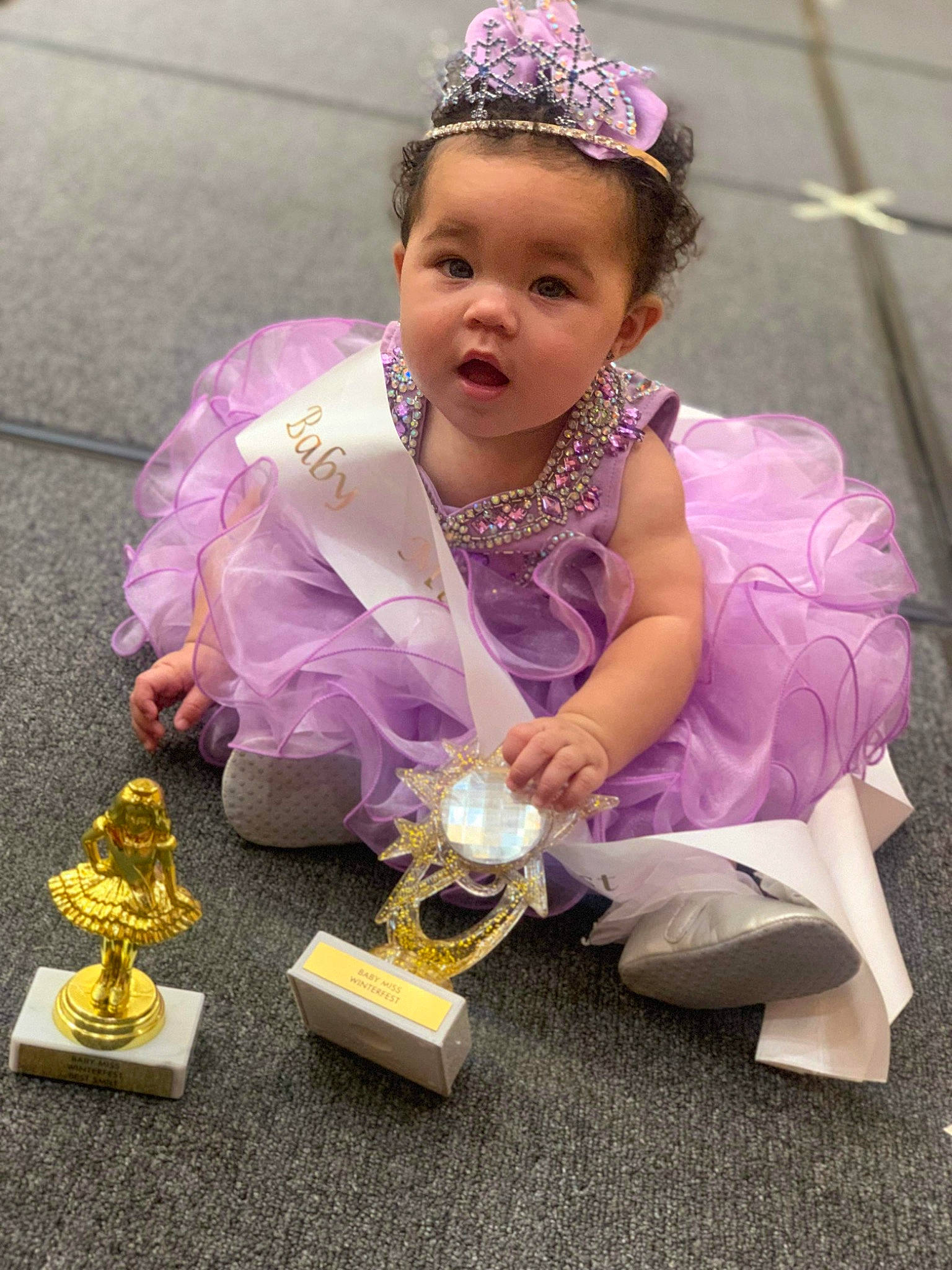 Arielle is registered to the contest to win money with this photo: baby, child, costume, dress, event, fashion_accessory, fun, happy, headband, headpiece, jewellery, magenta, necklace, person, pink, purple, sitting, tiara, toddler, toy