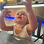 Lyzio participe au concours pour gagner de l'argent avec cette photo : toddler, child, white_tank_top, indoor, reaching, curious, blonde_hair, high_chair, table, face, expression, hands, portrait, young_child, casual_clothing, seat, looking_up, soft_lighting, shallow_depth_of_field, playful