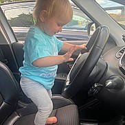 Lyzio a rejoint le concours — aidez-le/la à gagner de superbes lots ! child, toddler, car, steering_wheel, barefoot, blue_shirt, gray_pants, driver_seat, interior, window, daylight, playful, happy, person, seat, hand, foot, vehicle, inside, curious