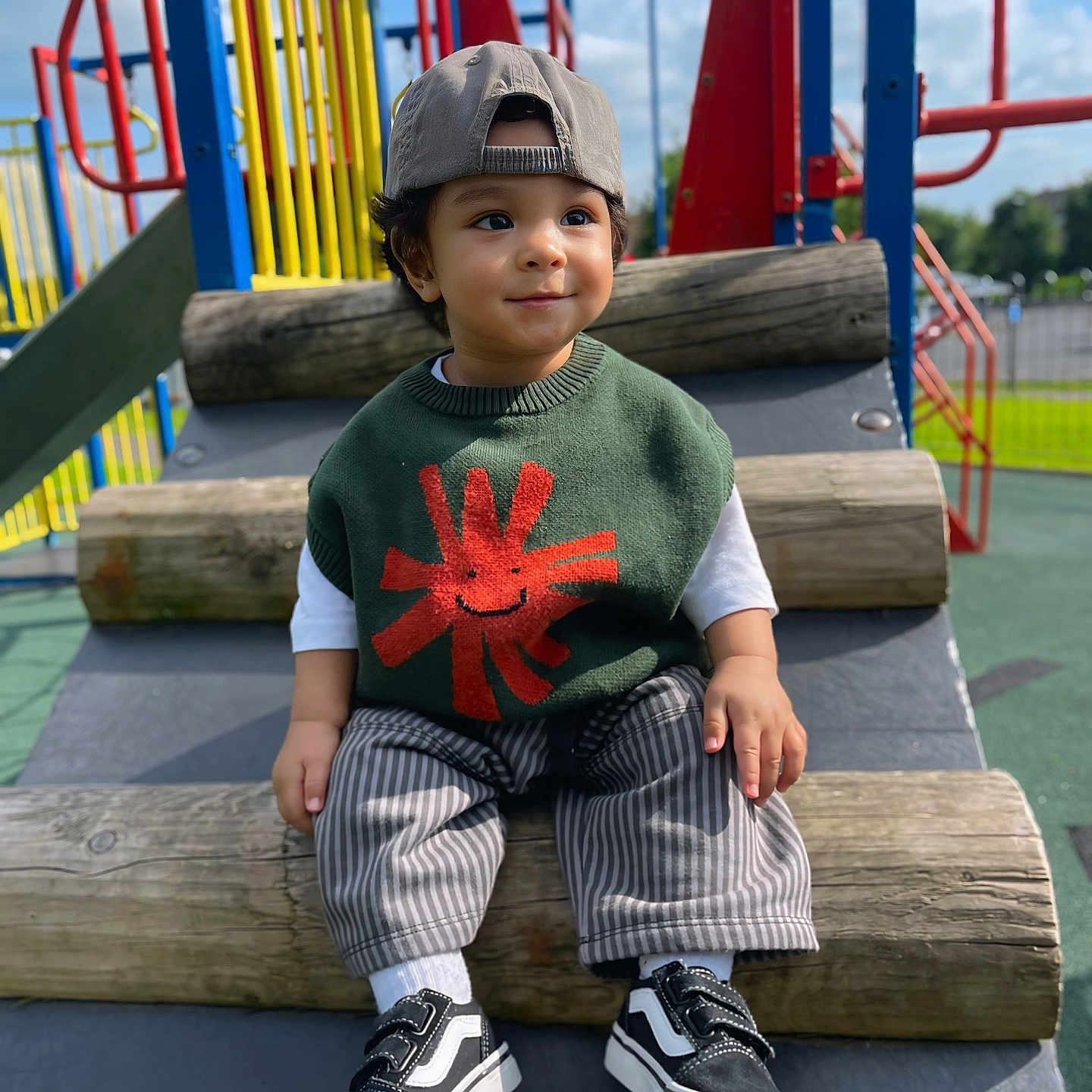 Kyzer is registered to the contest to win money with this photo: black_shoes, cap, casual_clothing, child, colorful, daylight, happy, outdoor, park, person, play_equipment, playground, shoes, smile, striped_pants, sunny, sweater, toddler, white_socks, wooden_logs