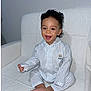 toddler, child, smiling, pajamas, striped_clothing, sitting, barefoot, curly_hair, indoor, armchair, white_chair, happy, portrait, baby, cute, young_child, comfortable, cozy, face, person