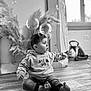 toddler, child, baby, sitting, indoor, black_and_white, bubbles, floor, wooden_floor, hoodie, pants, toy, window, plant, curious, hands, feet, face, expression, home