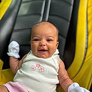 Skyla is registered to the contest to win money with this photo: baby, smiling, infant, white_mittens, pink_skirt, flower_pattern, black_cushion, yellow_cushion, seated, cute, happy, portrait, clothing, person, skin, face, head, photography, indoors, young_child