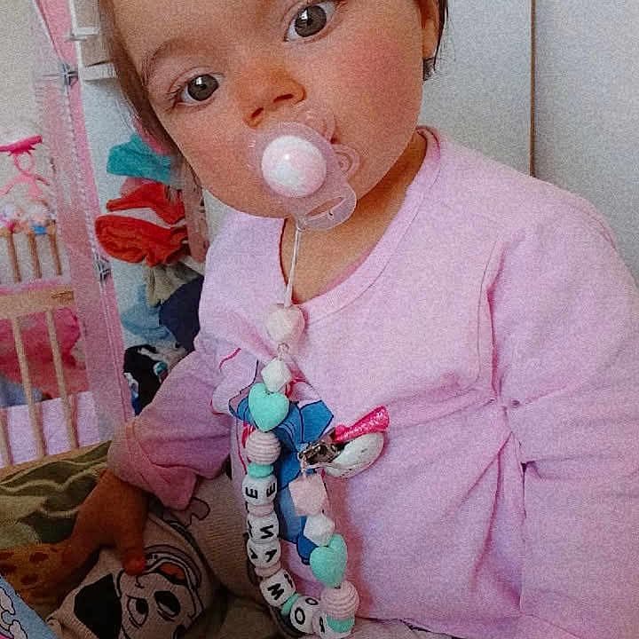 Romane participe au concours pour gagner de l'argent avec cette photo : toddler, child, pacifier, pink_clothing, patterned_pants, toy, blanket, indoor, cute, portrait, face, hand, hair_tie, sitting, young_child, baby_accessory, colorful, playful, home, curious