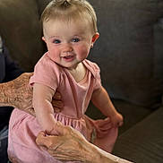 Raija joined the competition — help win amazing prizes! baby, child, toddler, smiling, portrait, indoor, living_room, couch, pink_dress, hair_bow, blue_eyes, sitting, standing, adult_hands, family, home, soft_lighting, blanket, furniture, happy