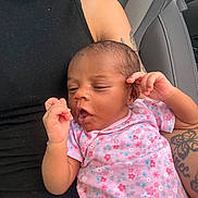 Anastasia is registered to the contest to win money with this photo: baby, infant, child, person, tattoo, car_seat, seatbelt, black_clothing, pink_onesie, floral_pattern, hand, face, skin, arm, denim, casual, portrait, indoors, relaxed, expression