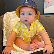Carter joined the competition — help win amazing prizes! baby, child, hat, bucket_hat, yellow_clothing, baby_seat, indoor, cute, chubby_cheeks, hands, feet, polo_logo, plaid_pattern, seated, portrait, infant, couch, painting, home, curious