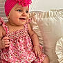 baby, child, smiling, pink_headband, flower, dress, floral_pattern, pillow, ruffled_pillow, cute, happy, indoors, seated, skin, hand, blue_eyes, infant, headwear, fabric, portrait