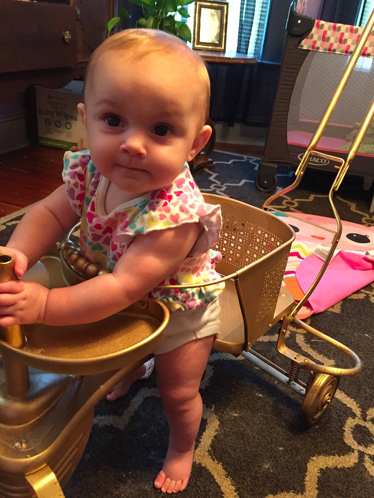 Sharon is registered to the contest to win money with this photo: baby, baby_toddler_clothing, bookcase, chair, child, event, floor, flooring, fun, human_leg, lap, person, picture_frame, sandal, sitting, skin, smile, television, thigh, tire