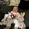 baby, child, smile, plush_toy, bunny, couch, pillow, stuffed_animal, indoor, happy, person, foot, clothing, knitwear, face, toy, seated, home, decor, infant